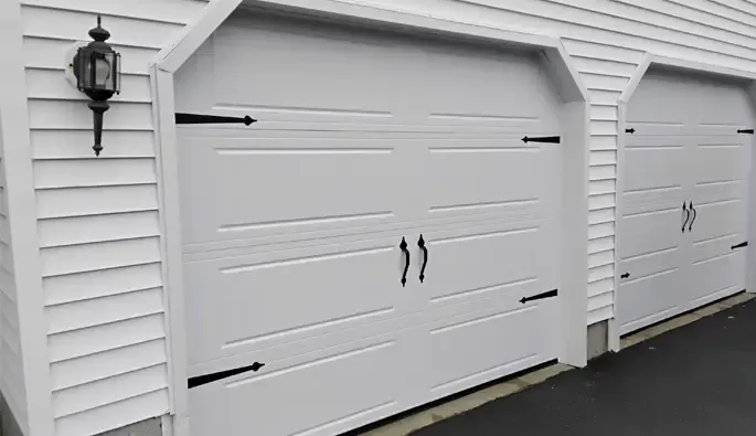 Two garage doors featuring white panels with black decorative hardware, positioned side by side.